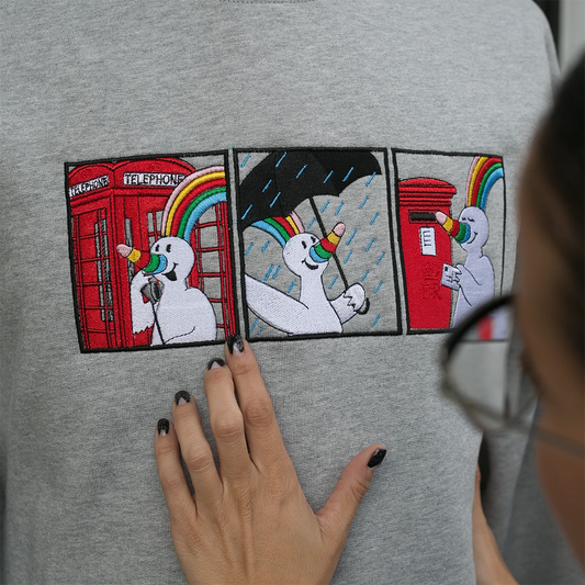 Manos de chica apreciendo el detalle del bordado Curro in London en sudadera gris.