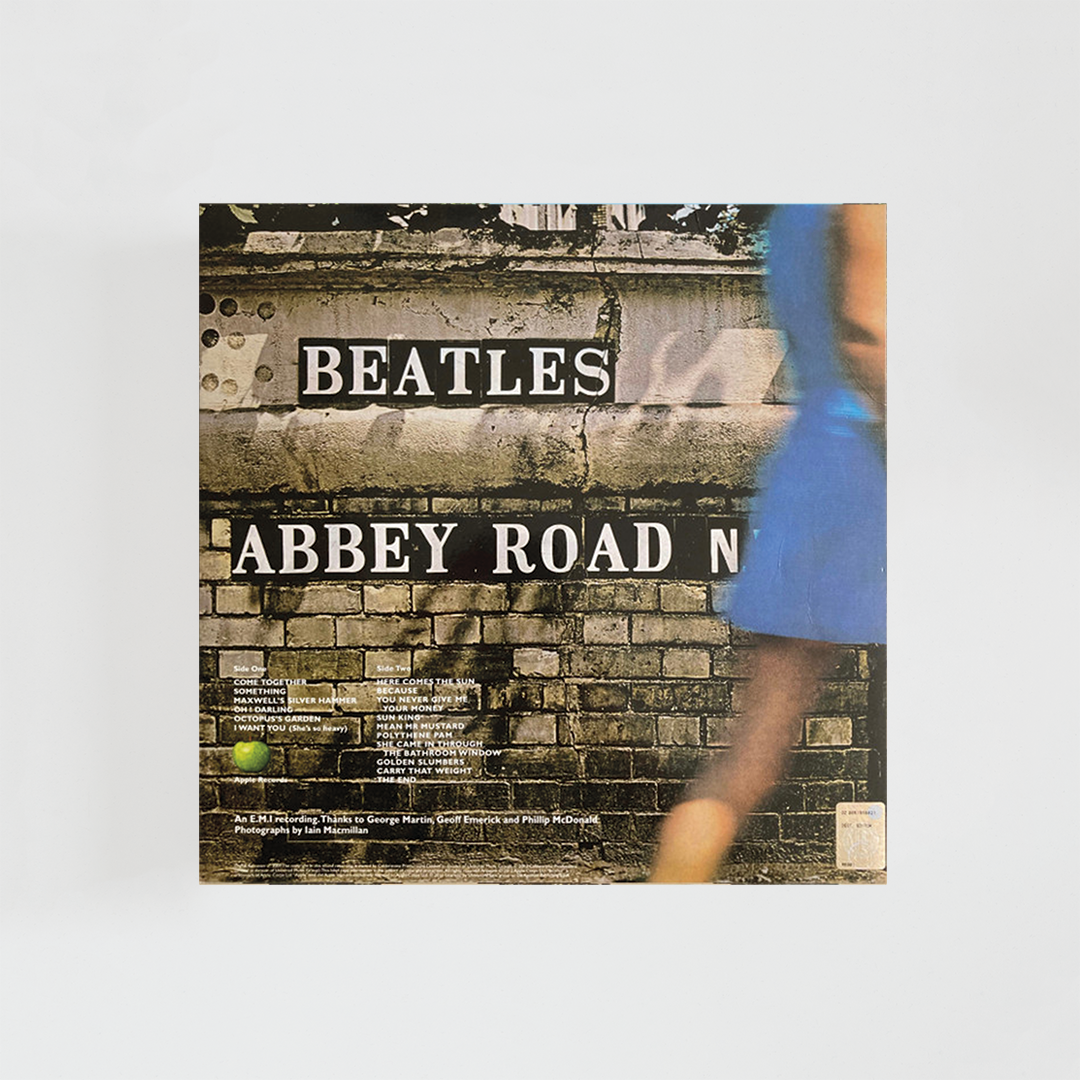 Contraportada del álbum “Abbey Road” de The Beatles, con la fachada de un edificio de ladrillo donde aparece pintado el título del disco junto a detalles urbanos y listados de créditos.