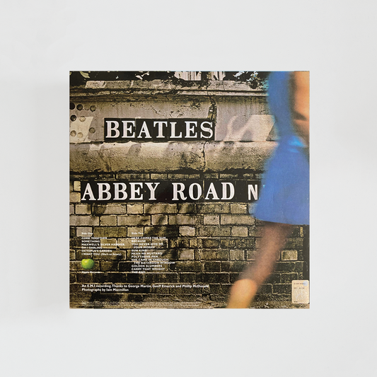 Contraportada del álbum “Abbey Road” de The Beatles, con la fachada de un edificio de ladrillo donde aparece pintado el título del disco junto a detalles urbanos y listados de créditos.