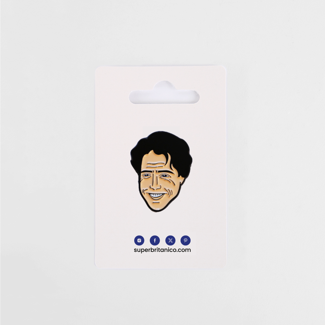 Pin con la ilustración de Hugh Grant a modo de caricatura. Predominan el color carne para la piel y el negro del pelo y rasgos de la cara. El packaging es una cartulina blanca con los logos azules de Superbritánico.