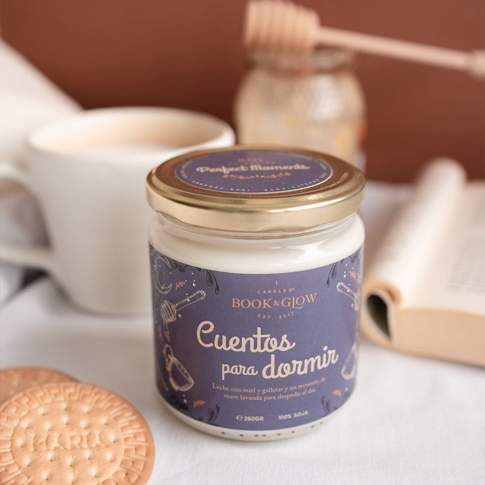 Vela de Book and Glow Cuentos para dormir presentada en recipiente de cristal cerrado, etiqueta azul con título en blanco sobre mesa.