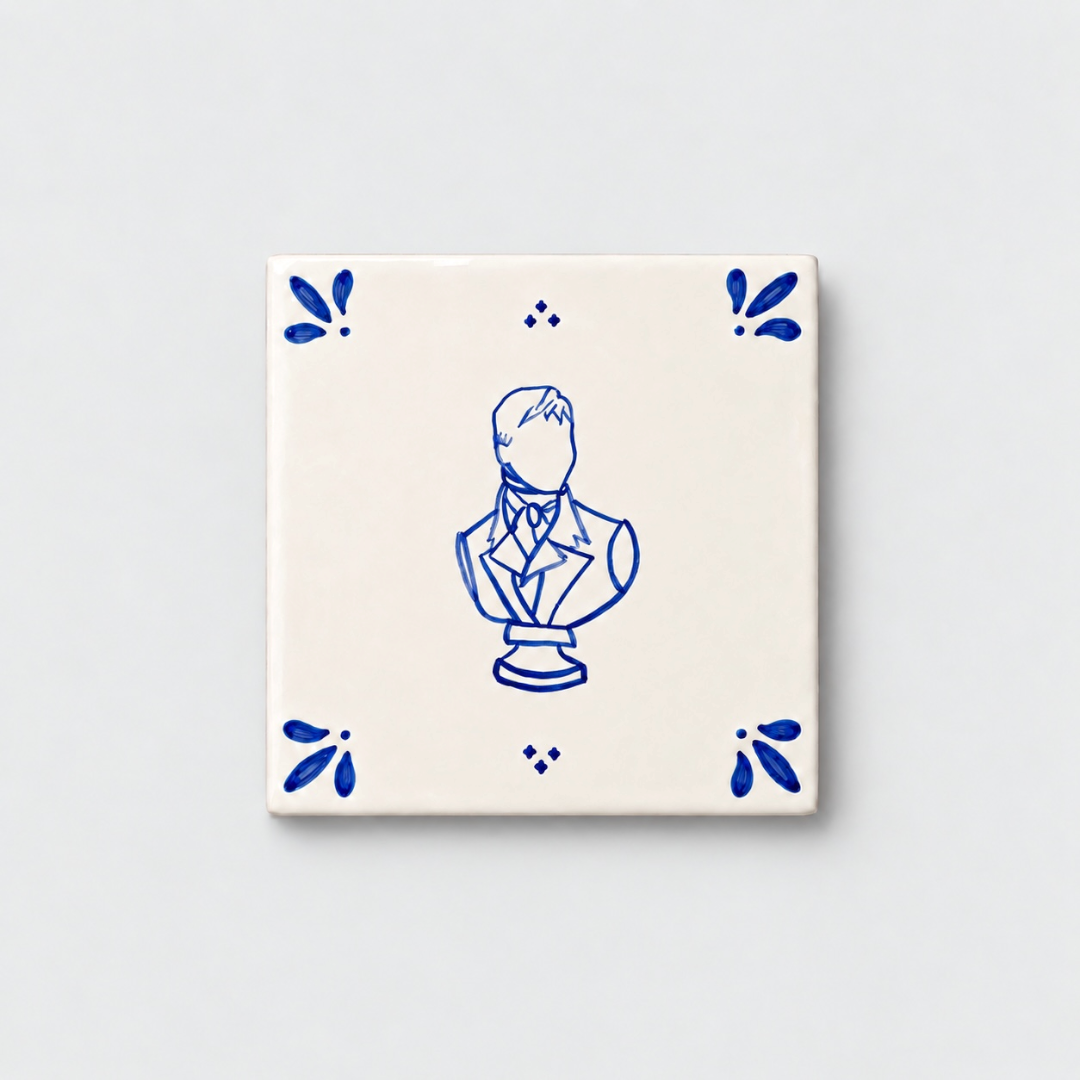 Azulejo decorativo de cerámica blanca con bordes y letras pintadas a mano en azul cobalto. En el centro tiene una ilustración del busto de Mr Darcy. El diseño incluye detalles ornamentales en las esquinas y pequeños puntos decorativos, sobre un fondo de pared blanca con textura rugosa.