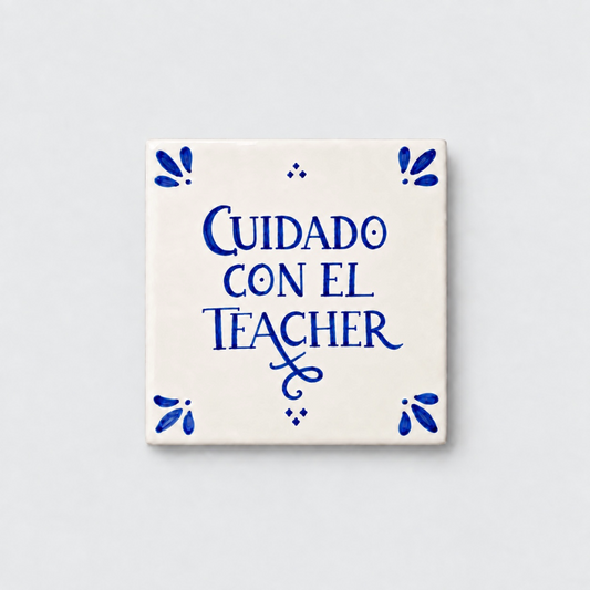 Azulejo decorativo de cerámica blanca con bordes y letras pintadas a mano en azul cobalto. En el centro se lee la frase en español 'CUIDADO CON EL TEACHER'. El diseño incluye detalles ornamentales en las esquinas y pequeños puntos decorativos, sobre un fondo de pared blanca con textura rugosa.