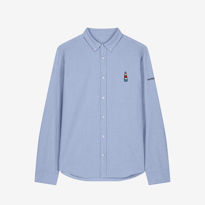 Camisa celeste de hombre con botones blancos y bordado pequeño de logo de incensario conmemorativo del cartel del Orgullo de Sevilla en pecho izquierdo.