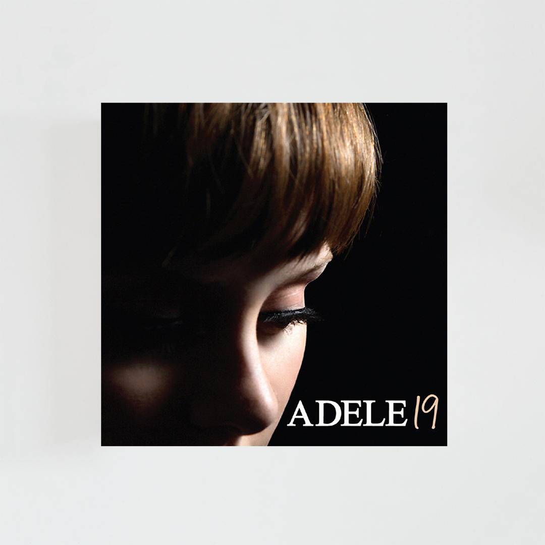 Portada del álbum 19 de Adele con un primer plano de la cantante de perfil, los ojos cerrados, el cabello oscuro cubriendo parte del rostro y fondo negro.