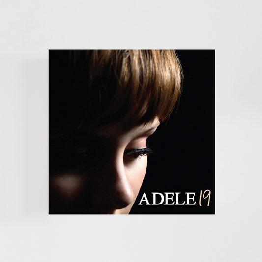 Portada del álbum 19 de Adele con un primer plano de la cantante de perfil, los ojos cerrados, el cabello oscuro cubriendo parte del rostro y fondo negro.
