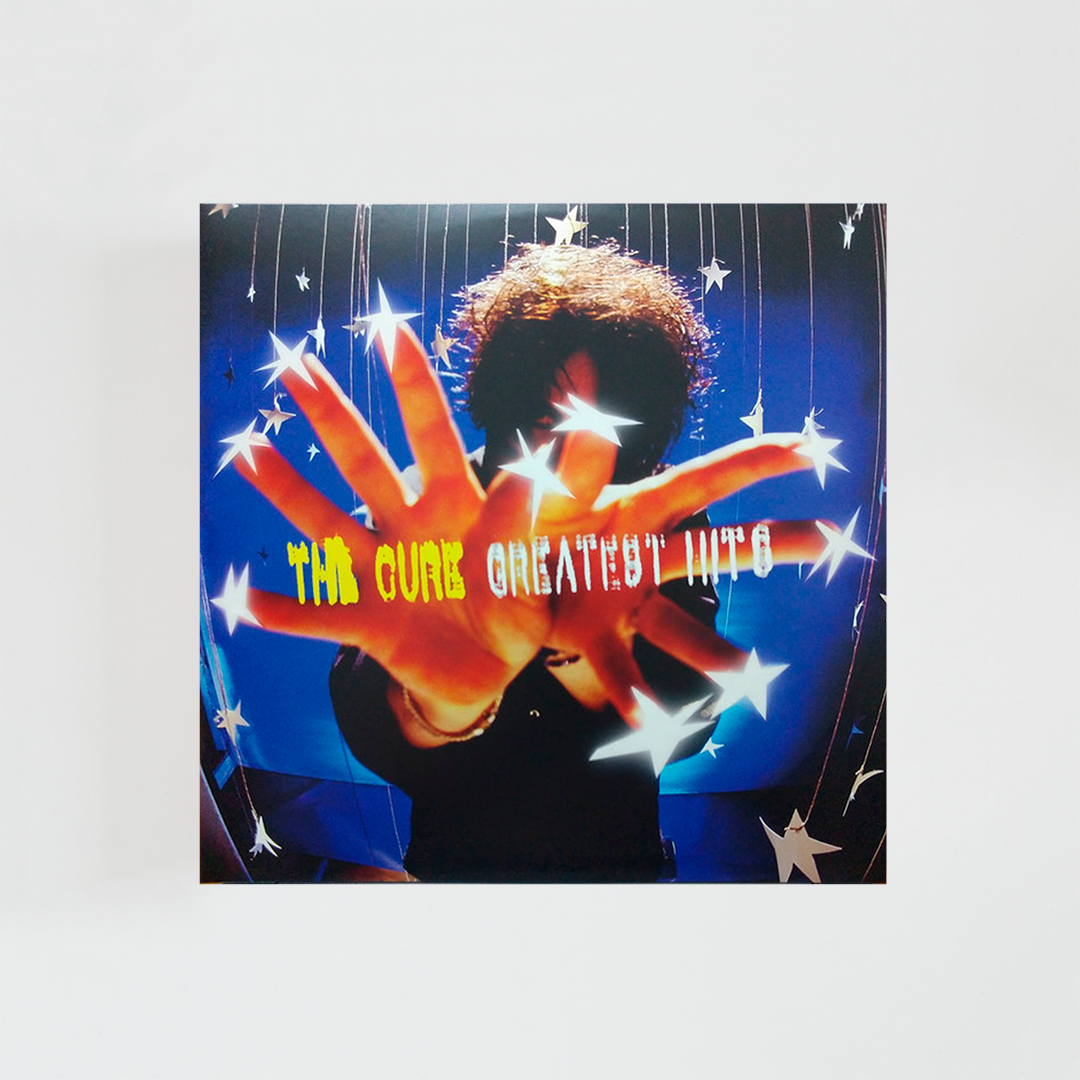 Portada del álbum “Greatest Hits” de The Cure, con la silueta de Robert Smith sobre un fondo estrellado, extendiendo las manos hacia la cámara mientras aparecen estrellas formando el título del disco.