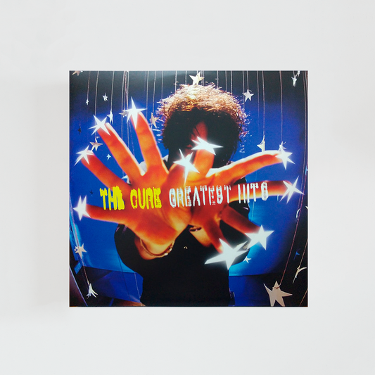 Portada del álbum “Greatest Hits” de The Cure, con la silueta de Robert Smith sobre un fondo estrellado, extendiendo las manos hacia la cámara mientras aparecen estrellas formando el título del disco.