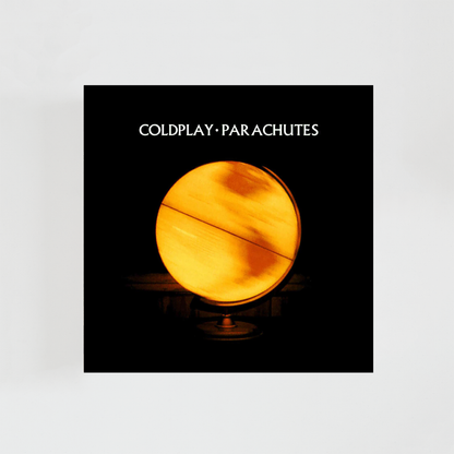 Portada del álbum Parachutes de Coldplay: fondo negro completamente oscuro con una imagen central en forma de fotografía esférica de la Tierra vista desde el espacio, iluminada de manera tenue y cálida. El planeta aparece pequeño y ligeramente desenfocado, con tonos amarillos y anaranjados suaves que contrastan con el negro profundo del fondo. La composición es minimalista, con mucho espacio vacío alrededor, transmitiendo sensación de aislamiento, calma y melancolía.