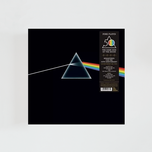 Portada del álbum The Dark Side of the Moon de Pink Floyd con un prisma sobre fondo negro que descompone un haz de luz blanca en un arcoíris. Esta edición incluye una banda vertical conmemorativa del 50.º aniversario.