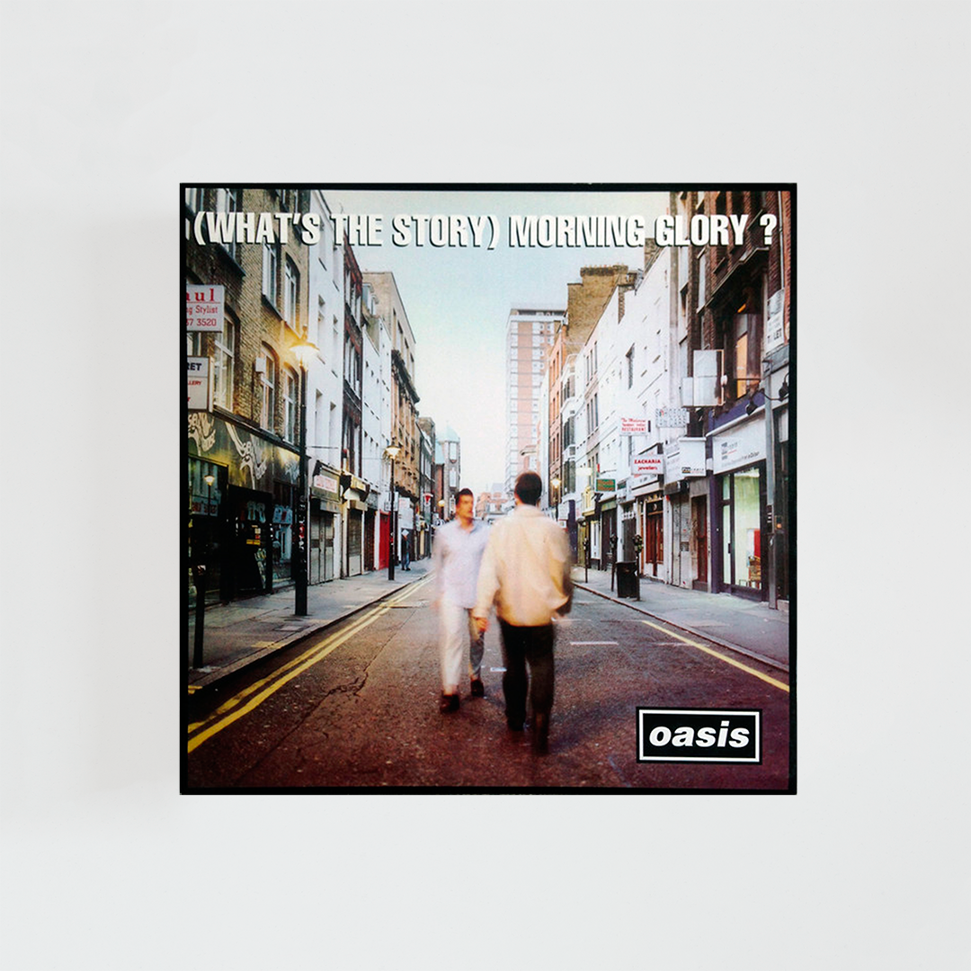 Portada del álbum “(What’s the Story) Morning Glory?” de Oasis, con los dos hermanos Gallagher caminando por la acera de una calle de Londres mientras dos transeúntes los observan, fotografía tomada de noche con iluminación urbana.