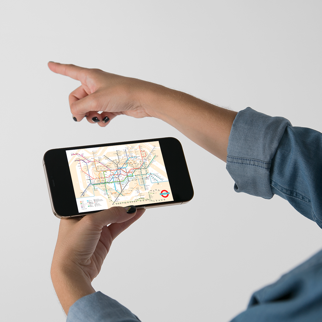 Chica señalando una dirección con una mano y con la otra sujetando el móvil con el mapa del metro de Londres de la guía digital de Londres Passport to London de Superbritánico.