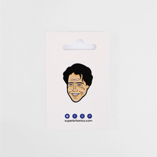 Pin con la ilustración de Hugh Grant a modo de caricatura. Predominan el color carne para la piel y el negro del pelo y rasgos de la cara. El packaging es una cartulina blanca con los logos azules de Superbritánico.