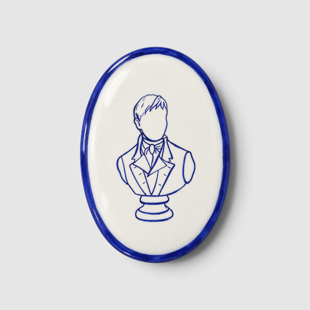 Placa ovalada de cerámica artesanal «Mr Darcy no existe» de Superbritánico, con ilustración del busto de Mr Darcy y borde pintados en azul cobalto sobre fondo blanco.