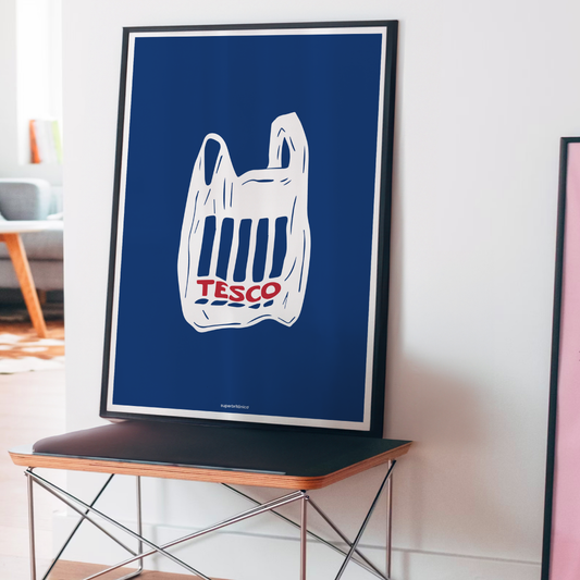 Póster ilustrado de Superbritánico con una bolsa de Tesco en blanco y rojo sobre fondo azul oscuro, apoyado sobre un mueble en un interior luminoso y moderno.