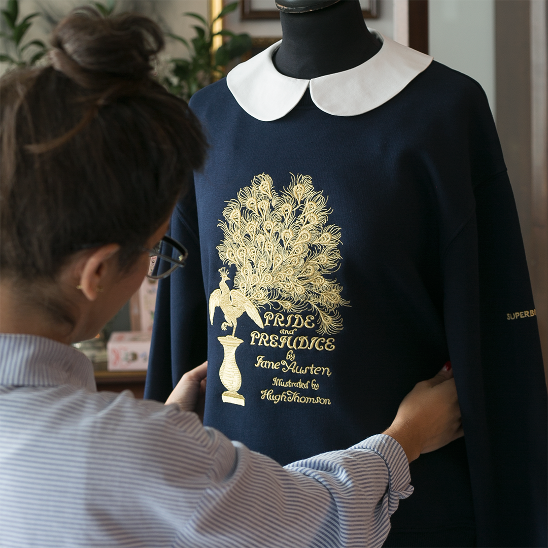 Sudadera color azul marino con bordado en dorado de la primera edición de la portada Pride and Prejudice de Jane Austen sobre maniquí.