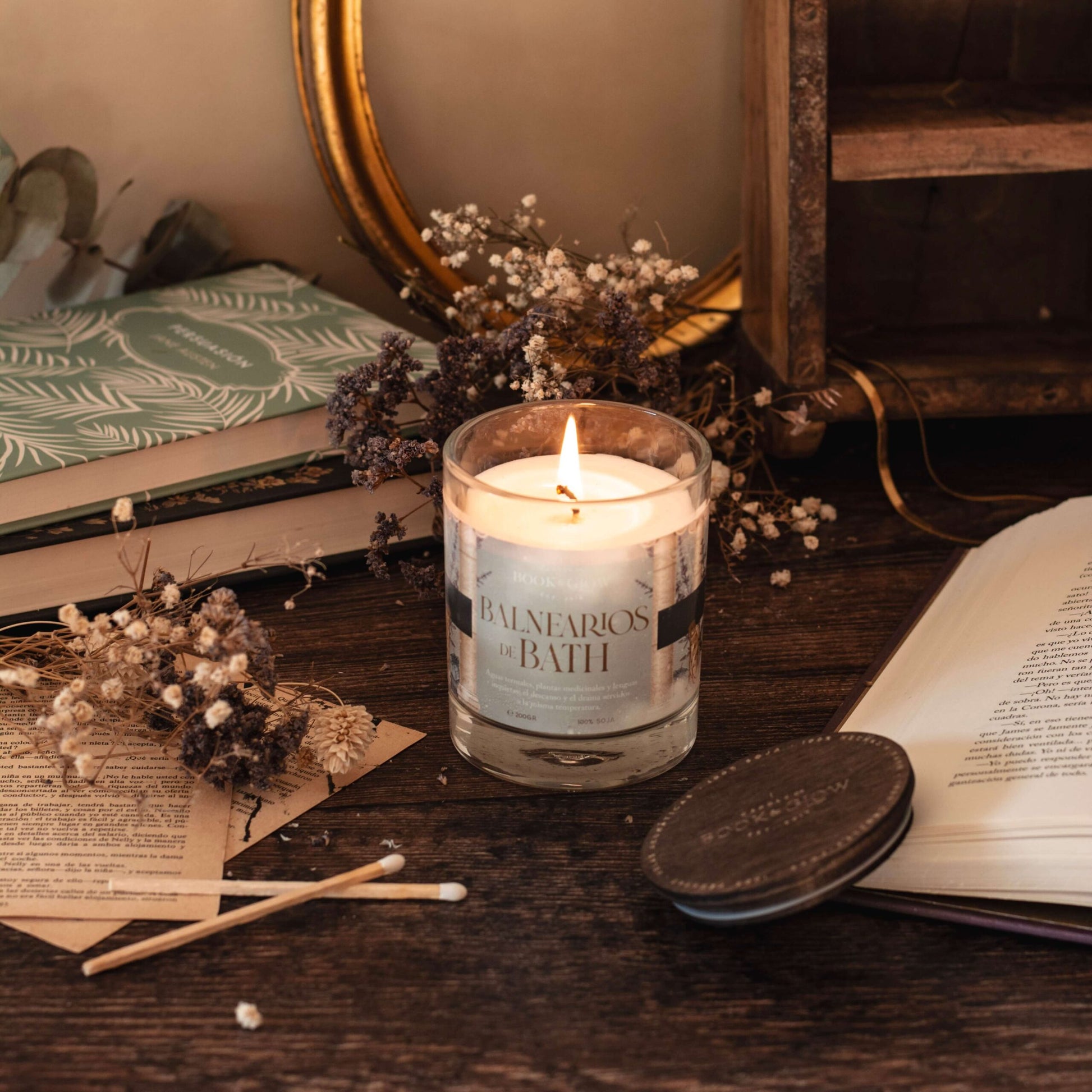 Vela Balnearios de Bath de Book and Glow encendida sobre escritorio de madera.