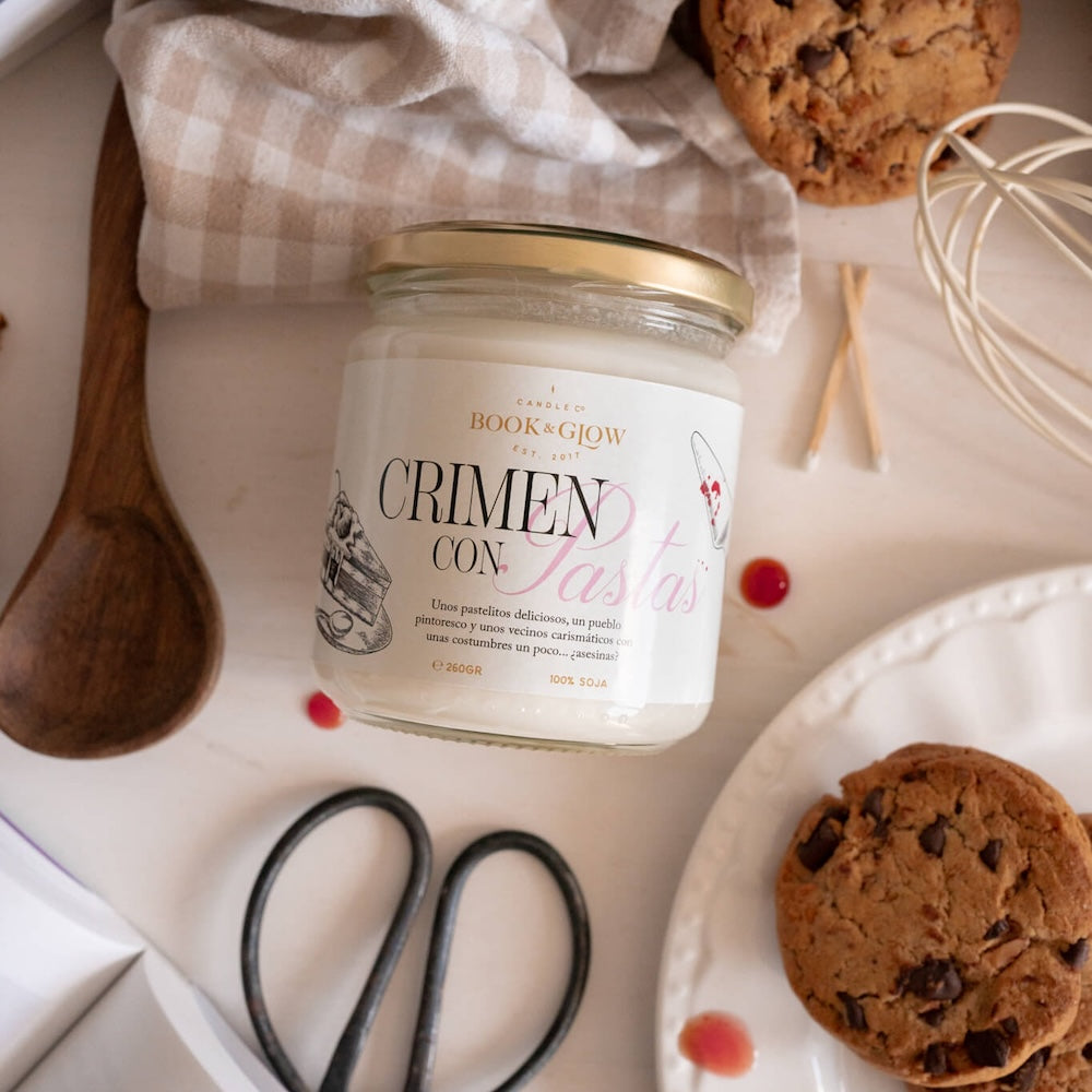 Vela de Book and Glow Crimen con pastas presentada en recipiente de cristal cerrado con etiqueta blanca y título en negro y rosa.
