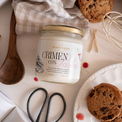 Vela de Book and Glow Crimen con pastas presentada en recipiente de cristal cerrado con etiqueta blanca y título en negro y rosa.