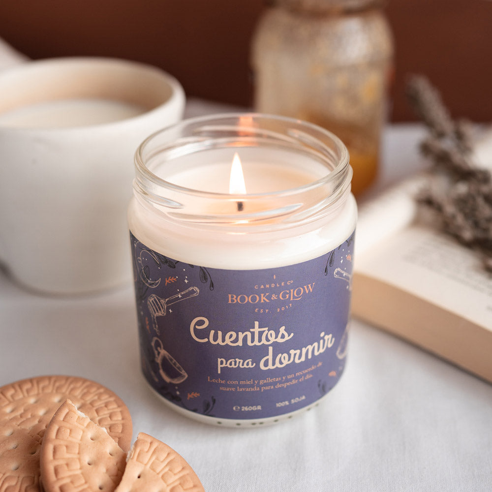 Vela de Book and Glow Cuentos para dormir presentada en recipiente de cristal, etiqueta azul con título en blanco sobre mesa.