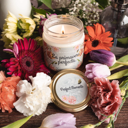 Vela La primavera perfecta de Book and Glow presentada abierta y encendida junto a bodegón de flores. La etiqueta de la vela es celeste con ilustraciones florales.