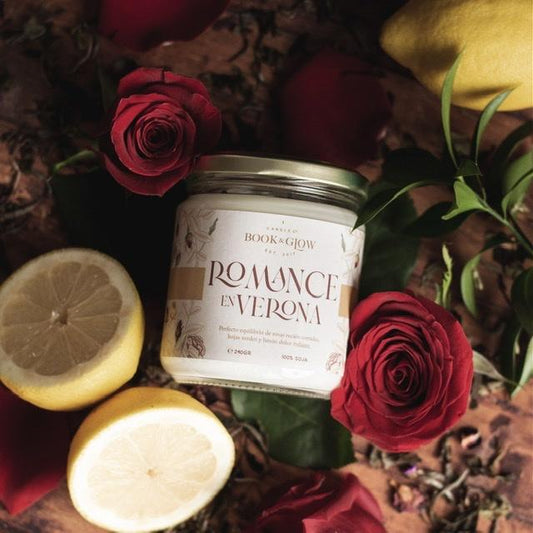 Vela de Book and Glow Romance en Verona presentada en recipiente de cristal con etiqueta blanca y título en beige, sobre mesa llena de rosas y limones.